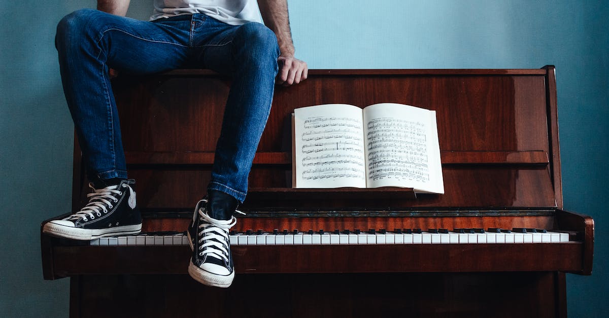 crop-unrecognizable-male-in-trendy-gumshoes-and-jeans-sitting-on-piano-with-sheet-music-in-classroom-4179352