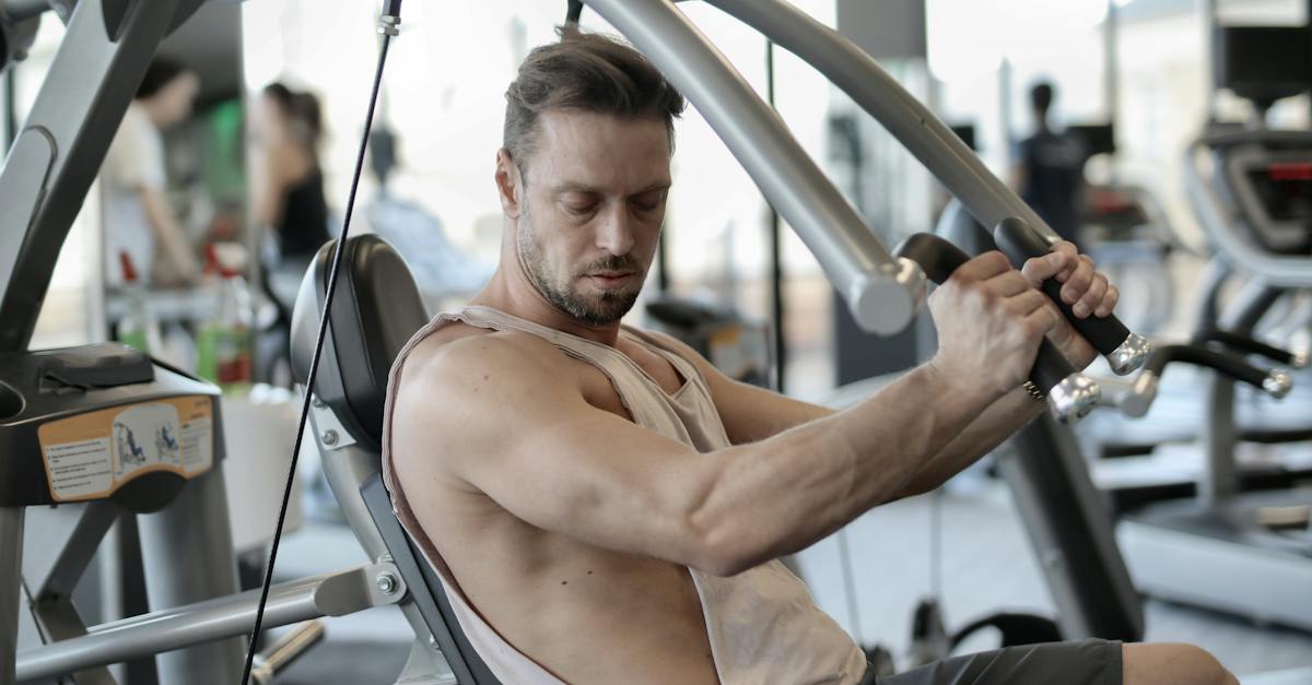 side-view-of-confident-muscular-man-doing-exercises-on-shoulder-press-machine-while-training-in-mode-8210879