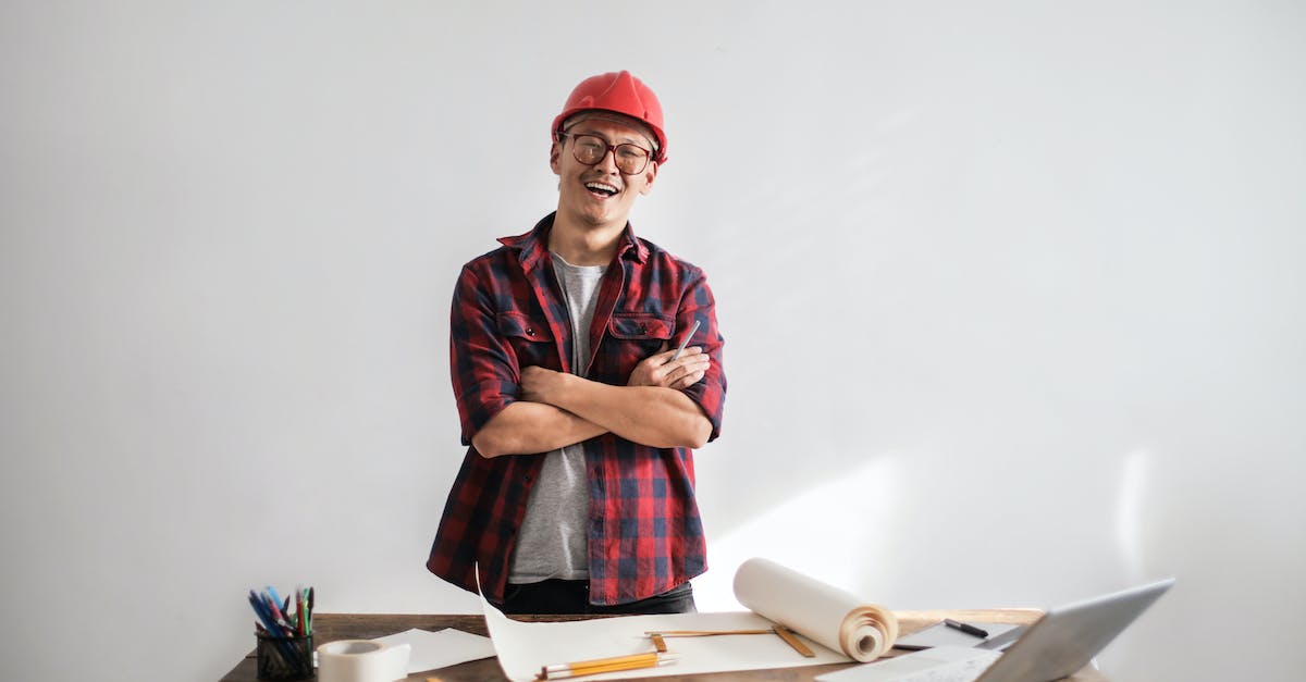 smiling-casual-man-in-hardhat-and-glasses-holding-arms-crossed-looking-at-camera-while-standing-at-d-8701097