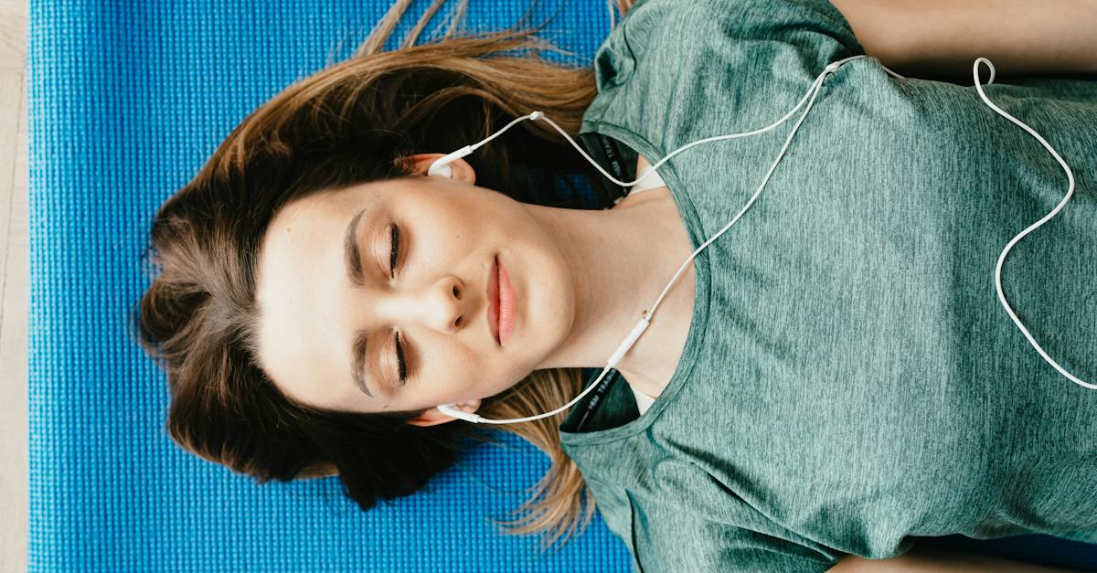 tranquil-woman-resting-on-yoga-mat-in-earphones-at-home-1558576