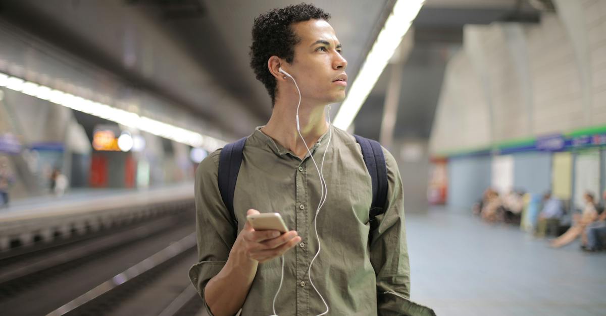 young-ethnic-man-in-earbuds-listening-to-music-while-waiting-for-transport-at-contemporary-subway-st-2086145