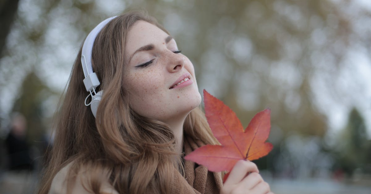 young-satisfied-woman-in-headphones-with-fresh-red-leaf-listening-to-music-with-pleasure-while-loung-3629269